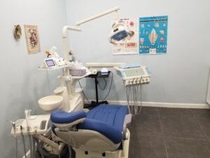 A close-up view of a dental work chair and equipment in an enclosed dental office at Crystal Bright Smile Dental Office in Tujunga, CA. The space is clean and well-lit, with a modern blue and white color motif. There are health posters on the walls.