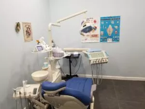 A close-up view of a dental work chair and equipment in an enclosed dental office at Crystal Bright Smile Dental Office in Tujunga, CA. The space is clean and well-lit, with a modern blue and white color motif. There are health posters on the walls.